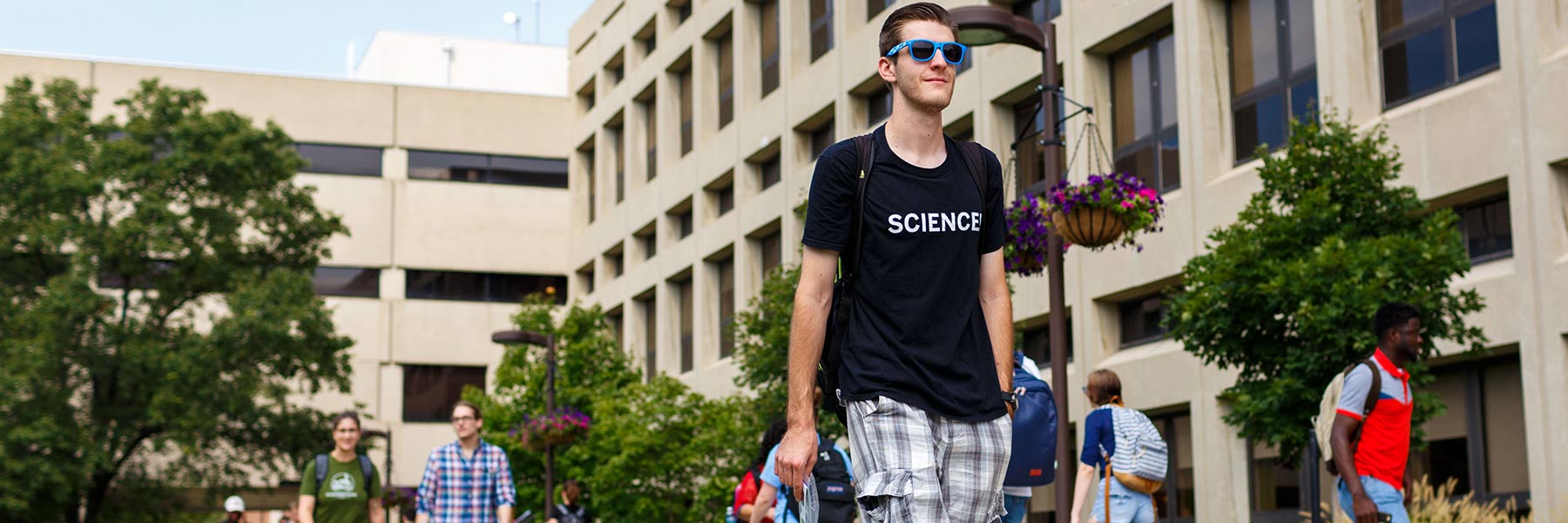 A student wearing sunglasses and a t-shirt that reads “SCIENCE” walks on campus.
