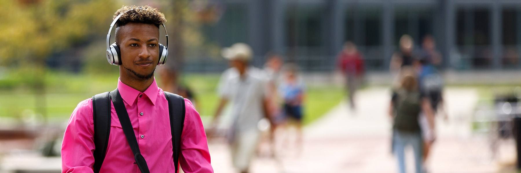 A student wearing headphones walks across campus.